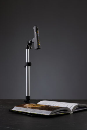 Billede af OrCam Read Læsestativ med en OrCam Read 3 i holderen, placeret over en åben bog