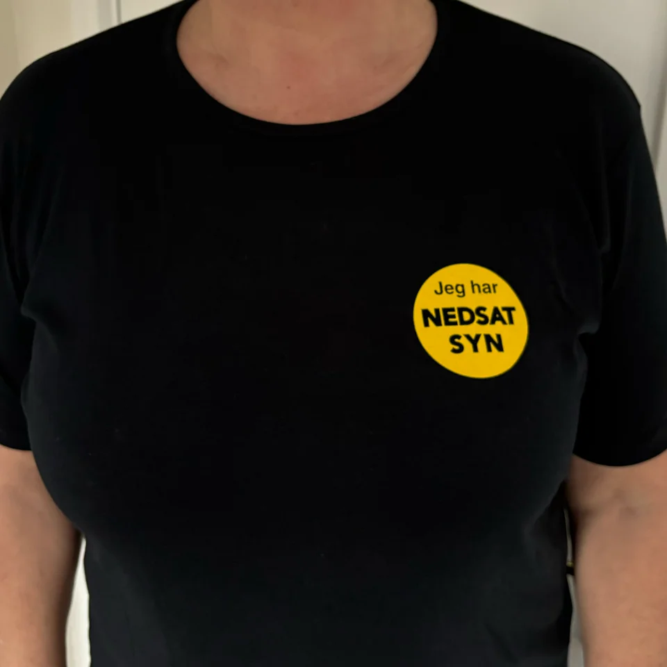 Billede af NEDSATSYN T-Shirt til herre eller dame, sort t-shirt med gult, rundt område på venstre bryst, med teksten Jeg har nedsat syn