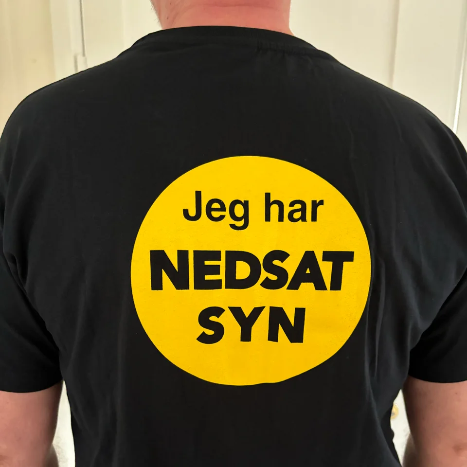 Billede af NEDSATSYN T-shirt set bagfra, med gult område med teksten Jeg har nedsat syn