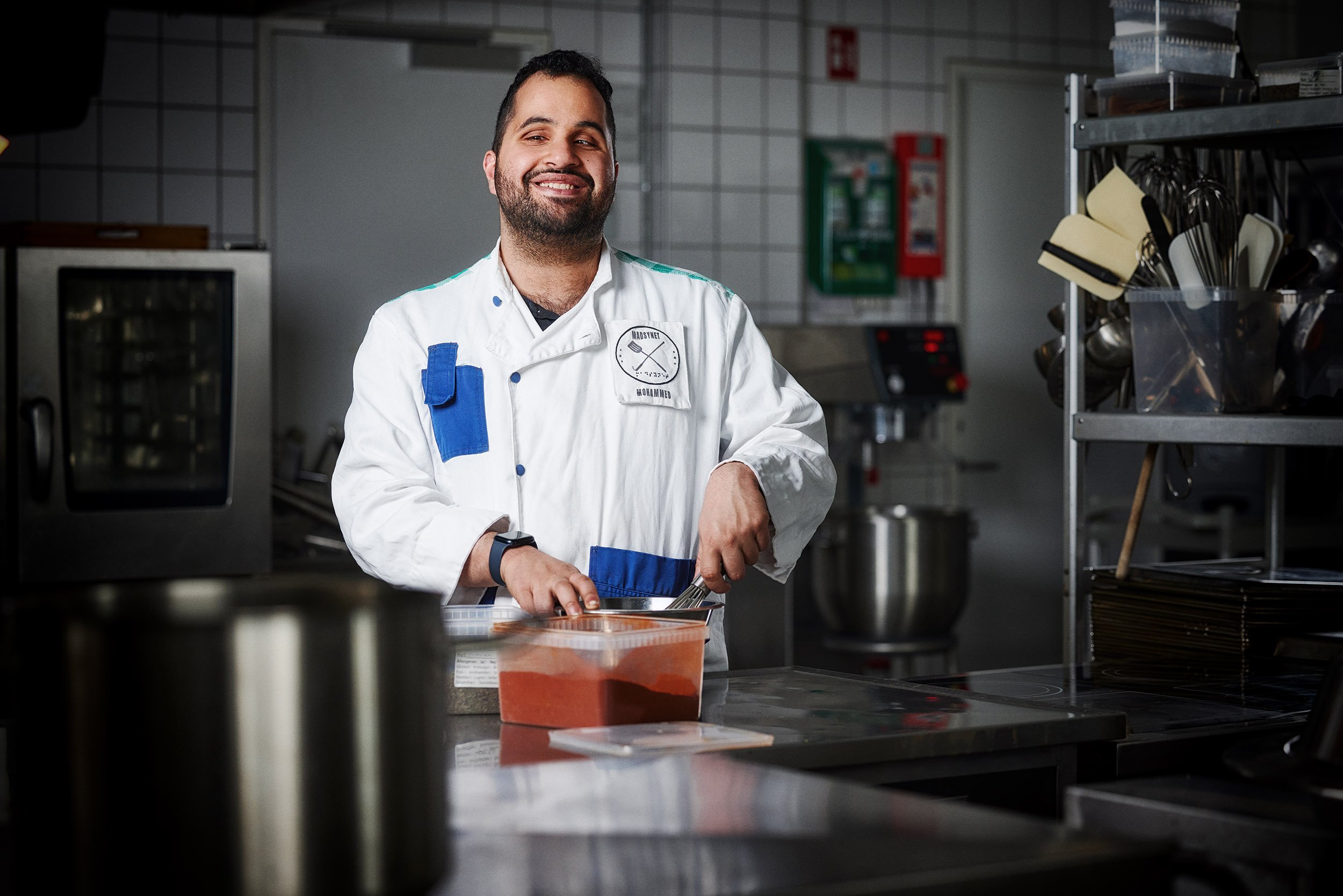 Billede af Mohammed Alsaadi i et køkken med køkkeuniform i gang med at blande ingredienser Billede af Mohammed Alsaadi i et køkken med køkkeuniform i gang med at blande ingredienser