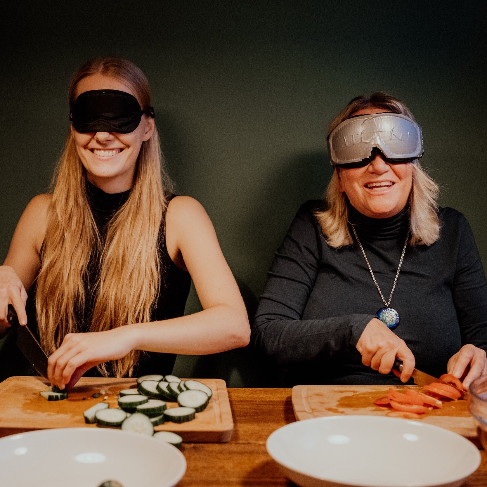 Billede fra Madsynet af to personer med bind for øjene som sidder foran spækbræt i gang med at skære grøntsager Billede fra Madsynet af to personer med bind for øjene som sidder foran spækbræt i gang med at skære grøntsager