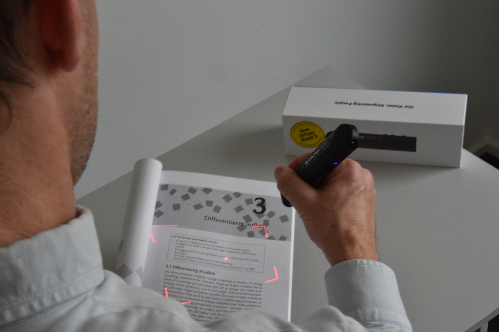 Billede af OrCam Read 3 som person bruger til at læse en side i en bog Billede af OrCam Read 3 som person bruger til at læse en side i en bog