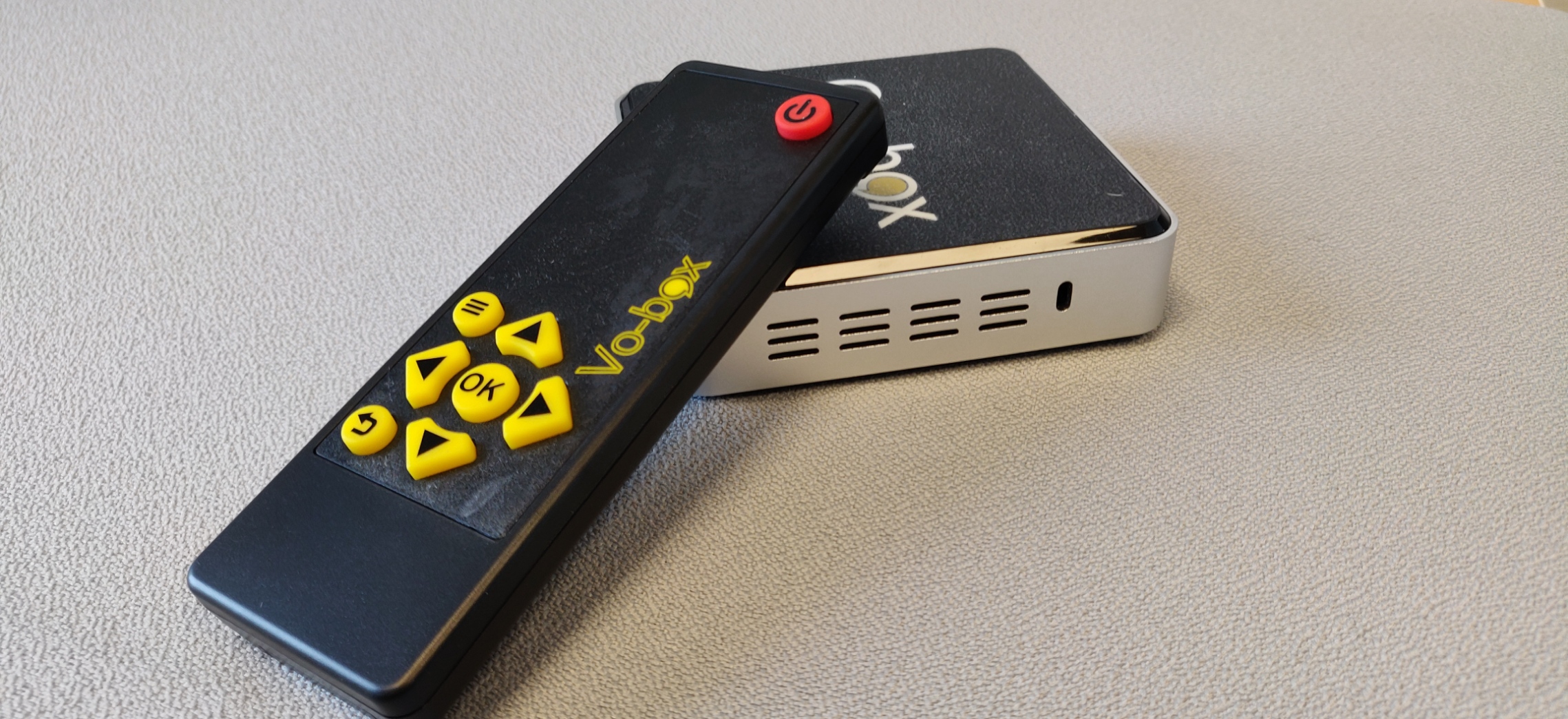 Billede af fjernbetjening til Vo-box placeret oven på en Vo-box enhed